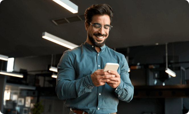 Man smiling while using smartphone in a modern office.